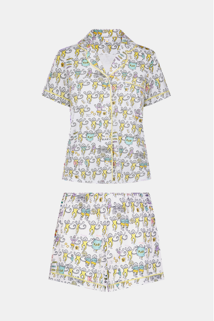 The Kappa Alpha Theta Monkey Polo Pajamas from Roller Rabbit are a short-sleeve button-up set with matching shorts, showcasing a lively print of colorful cartoon monkeys and doodles on a crisp white background. They feature an elastic waistband for comfort and are crafted from soft Pima cotton for a gentle feel.