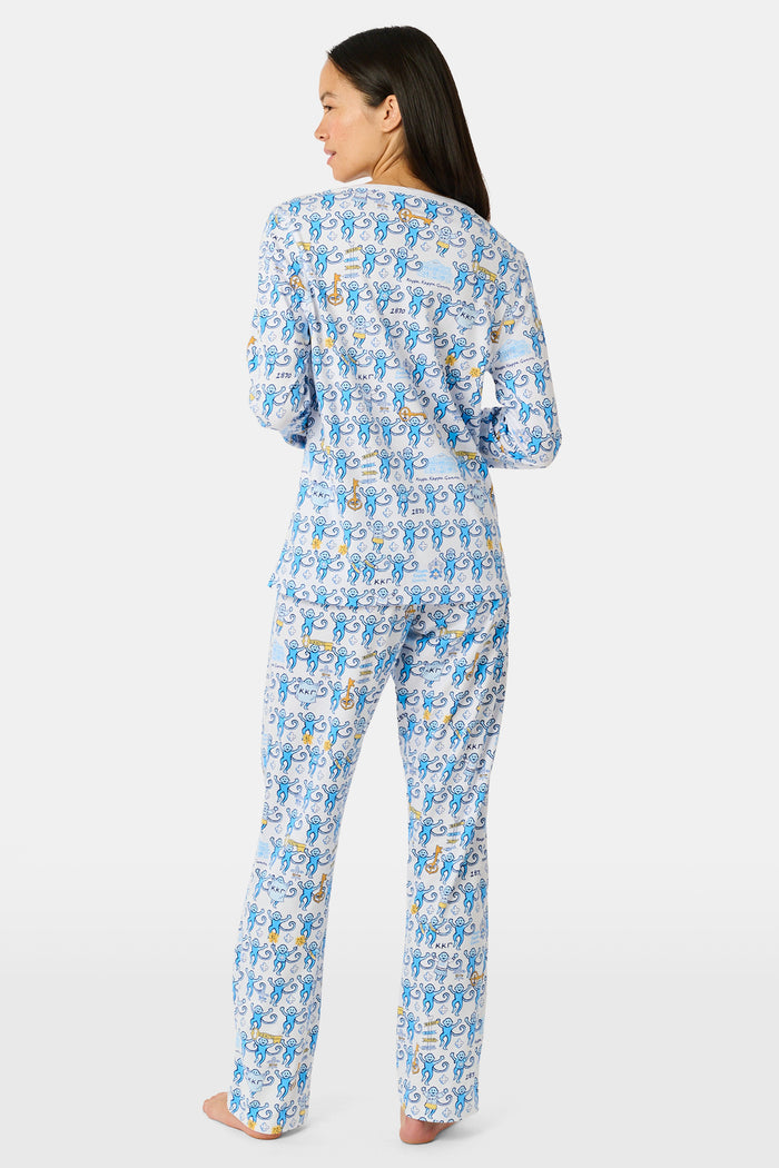 The Roller Rabbit Kappa Kappa Gamma Monkey Pajamas are a two-piece set with long sleeves and pants, showcasing an all-over blue and yellow monkey cartoon print on a white background, displayed on a flat white backdrop.