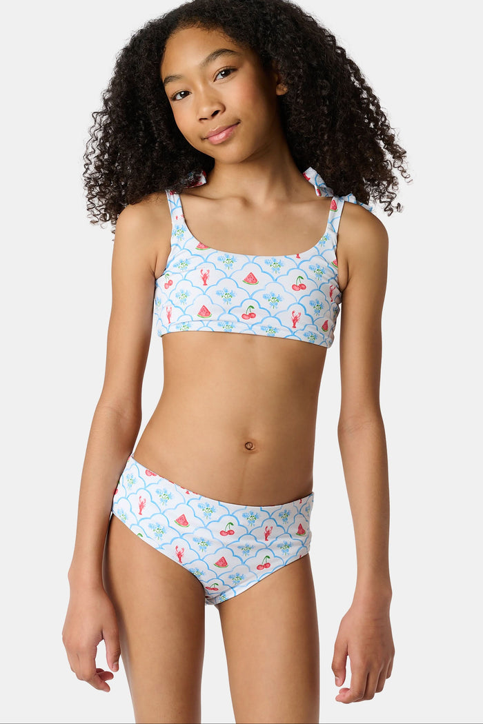 A young girl with curly hair wears the Roller Rabbit Kids 4th Of Jemina/Starry Dot Cora Bikini. She stands against a plain light gray background, looking at the camera with a slight smile.