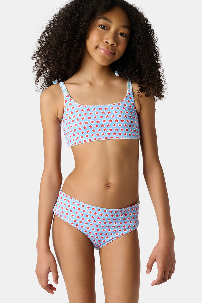 A young girl with curly hair wears the Roller Rabbit Kids 4th Of Jemina/Starry Dot Cora Bikini. She stands against a plain light gray background, looking at the camera with a slight smile.