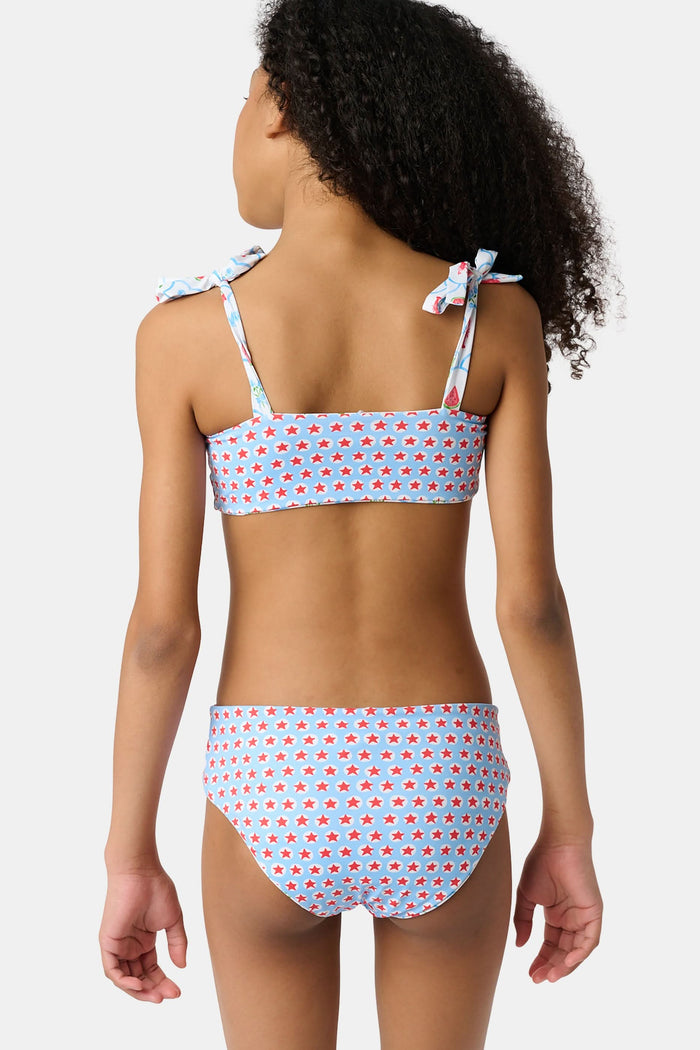A young girl with curly hair wears the Roller Rabbit Kids 4th Of Jemina/Starry Dot Cora Bikini. She stands against a plain light gray background, looking at the camera with a slight smile.