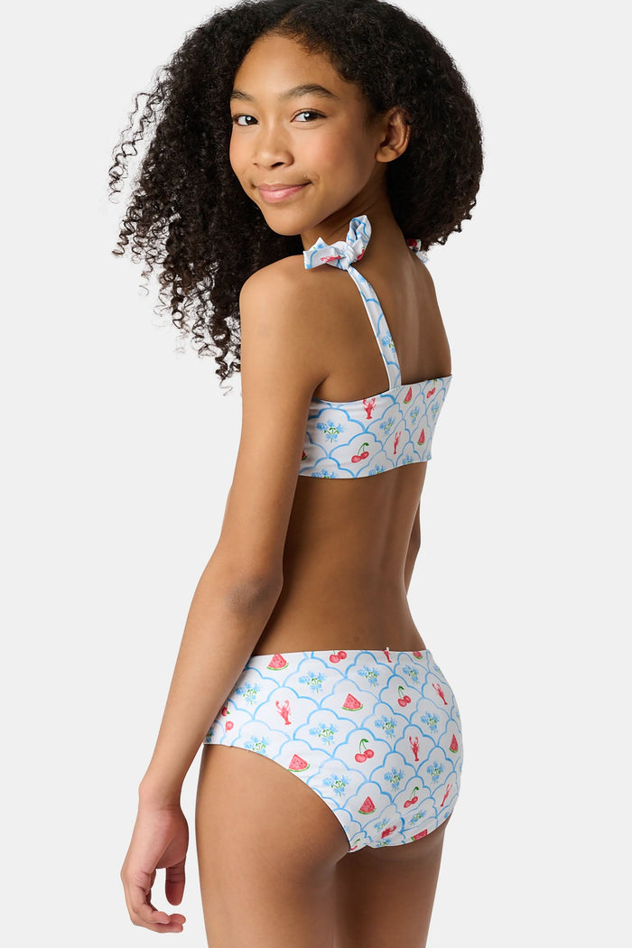 A young girl with curly hair wears the Roller Rabbit Kids 4th Of Jemina/Starry Dot Cora Bikini. She stands against a plain light gray background, looking at the camera with a slight smile.
