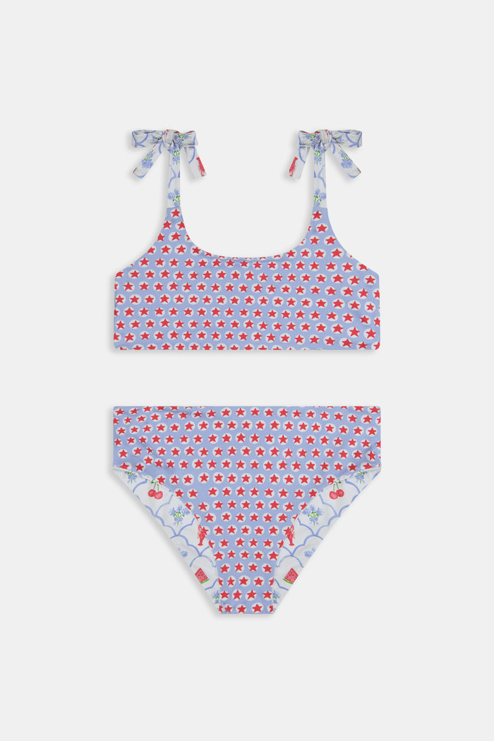 A young girl with curly hair wears the Roller Rabbit Kids 4th Of Jemina/Starry Dot Cora Bikini. She stands against a plain light gray background, looking at the camera with a slight smile.