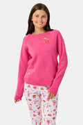 A young girl smiles, wearing the Roller Rabbit Kids Autumn Hearts Crewneck—a pink sweatshirt featuring small embroidered butterflies—paired with a white skirt adorned with a colorful heart pattern, as she stands with her hands behind her back.