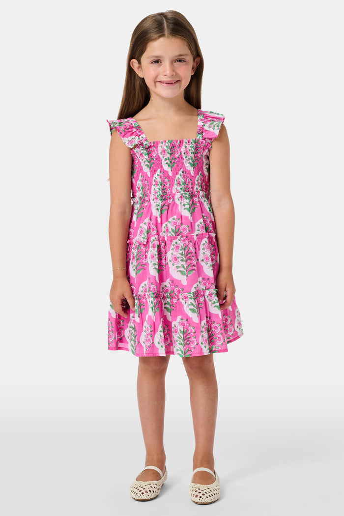 The Kids Ava Floral Ceri Dress by Roller Rabbit is a sleeveless baby dress featuring a smocked bodice and ruffled straps, adorned with green and white leaf patterns on a vibrant pink background, and comes with matching bloomers.