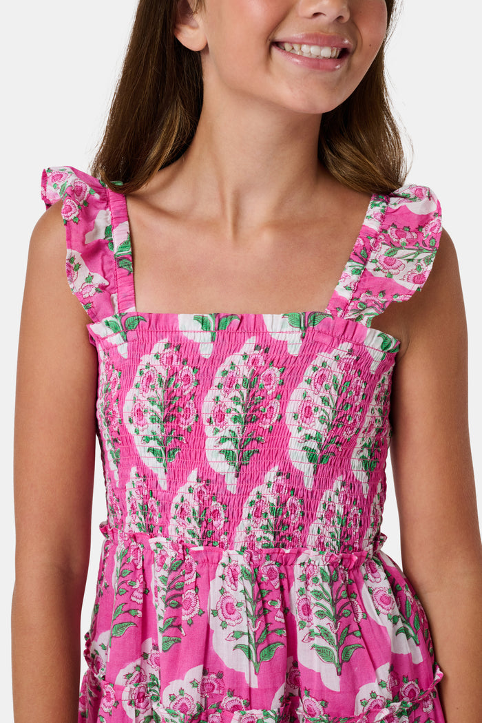 The Kids Ava Floral Ceri Dress by Roller Rabbit is a sleeveless baby dress featuring a smocked bodice and ruffled straps, adorned with green and white leaf patterns on a vibrant pink background, and comes with matching bloomers.