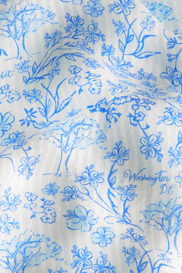 A woman stands barefoot in the Roller Rabbit Cherry Blossom Toile Liza Set—light blue and white cherry blossom print pajama pants with a matching short-sleeved, collared, button-up shirt—against a plain white background.