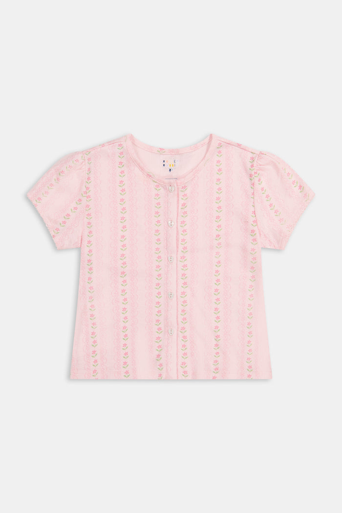 A young girl in a rose pink dress smiles while kneeling on the floor, holding a colorful folder. A pink backpack hangs nearby in a classroom or locker area, and she wears her cozy Roller Rabbit Kids Daisy Heart Stripe Diana Cardigan.