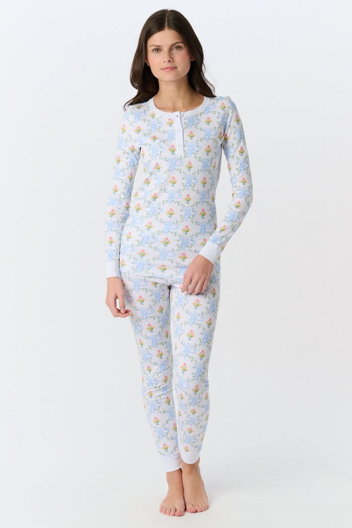 A child in Kids Floral Monkey Trellis Pajamas by Roller Rabbit sits barefoot on an adult’s lap outdoors. The adult, also barefoot and wearing light blue Pima Cotton sleepwear, hugs the child gently; only part of them is visible.