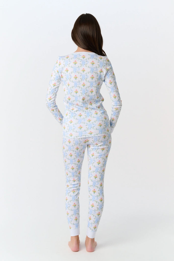 A child in Kids Floral Monkey Trellis Pajamas by Roller Rabbit sits barefoot on an adult’s lap outdoors. The adult, also barefoot and wearing light blue Pima Cotton sleepwear, hugs the child gently; only part of them is visible.