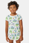 A girl stands outdoors in a Roller Rabbit Kids Game, Set, Monkey Playa Play Set, holding out a tennis ball toward the camera. Her playful outfit is perfect for kids’ tennis activities, and the photo is taken from a low angle with blue sky and trees in the background.