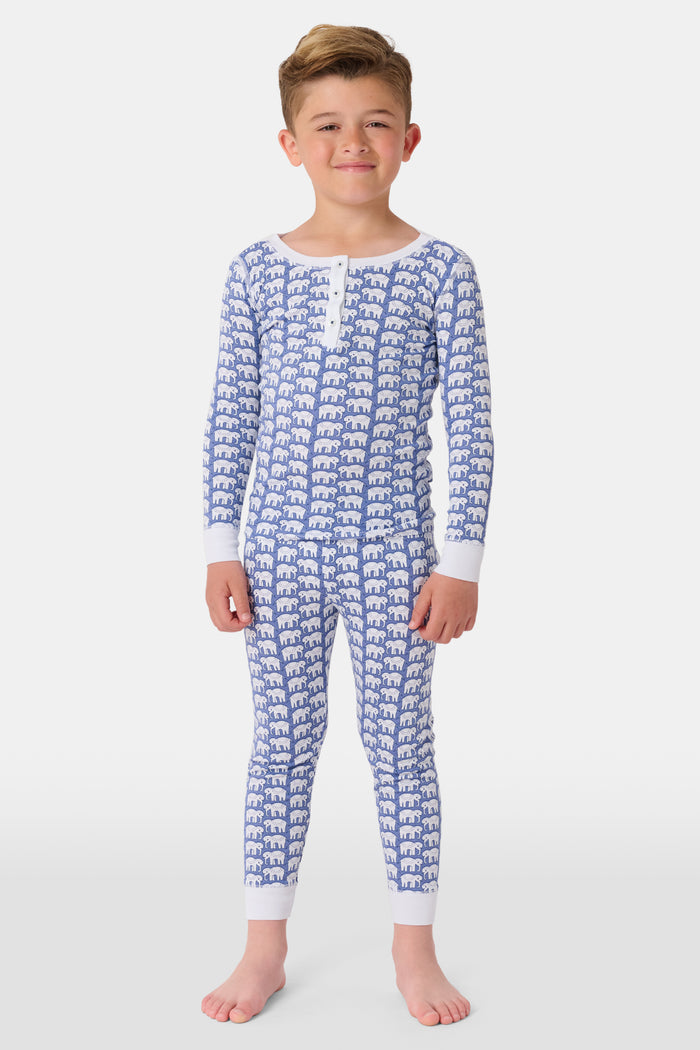 A young boy stands barefoot, smiling in Roller Rabbit Kids Hathi Pajamas—a matching Pima Cotton set with blue elephant print and white cuffs—against a plain white background.
