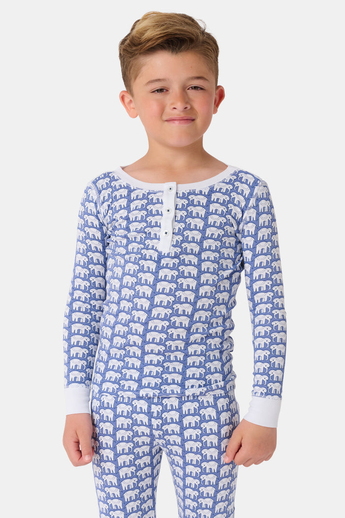 A young boy stands barefoot, smiling in Roller Rabbit Kids Hathi Pajamas—a matching Pima Cotton set with blue elephant print and white cuffs—against a plain white background.
