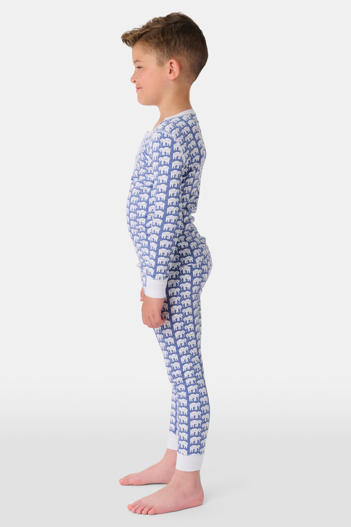 A young boy stands barefoot, smiling in Roller Rabbit Kids Hathi Pajamas—a matching Pima Cotton set with blue elephant print and white cuffs—against a plain white background.