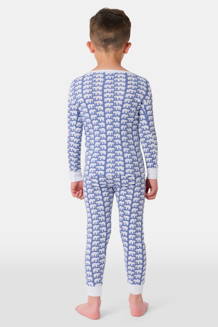 A young boy stands barefoot, smiling in Roller Rabbit Kids Hathi Pajamas—a matching Pima Cotton set with blue elephant print and white cuffs—against a plain white background.