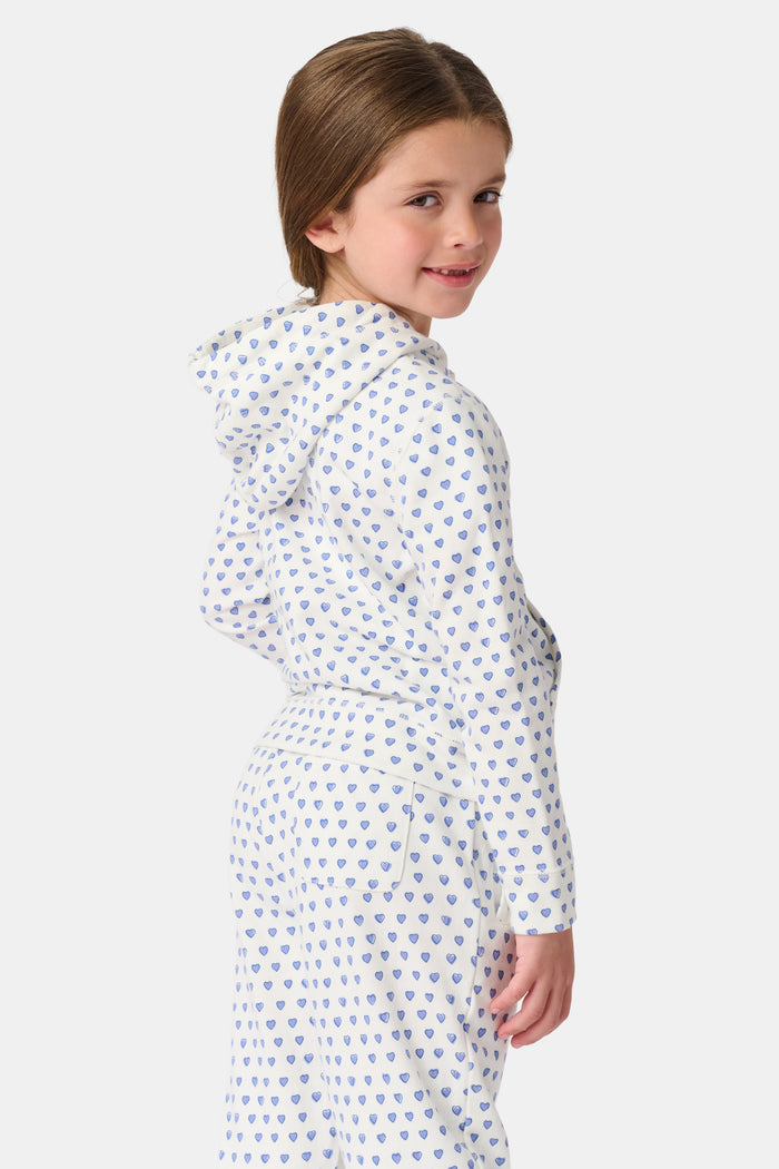 A smiling young child with brown hair wears the Roller Rabbit Kids Hearts Harley Hoodie and matching pants, both made from 100 cotton French terry, standing with hands in the hoodie’s pockets against a plain light background.