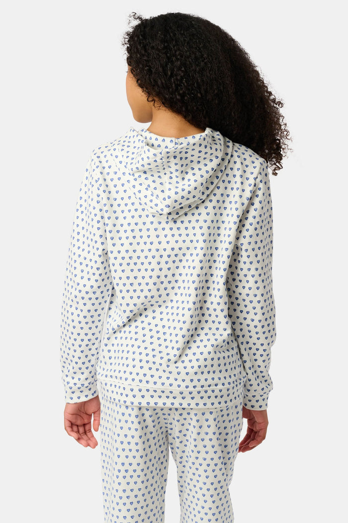 A smiling young child with brown hair wears the Roller Rabbit Kids Hearts Harley Hoodie and matching pants, both made from 100 cotton French terry, standing with hands in the hoodie’s pockets against a plain light background.
