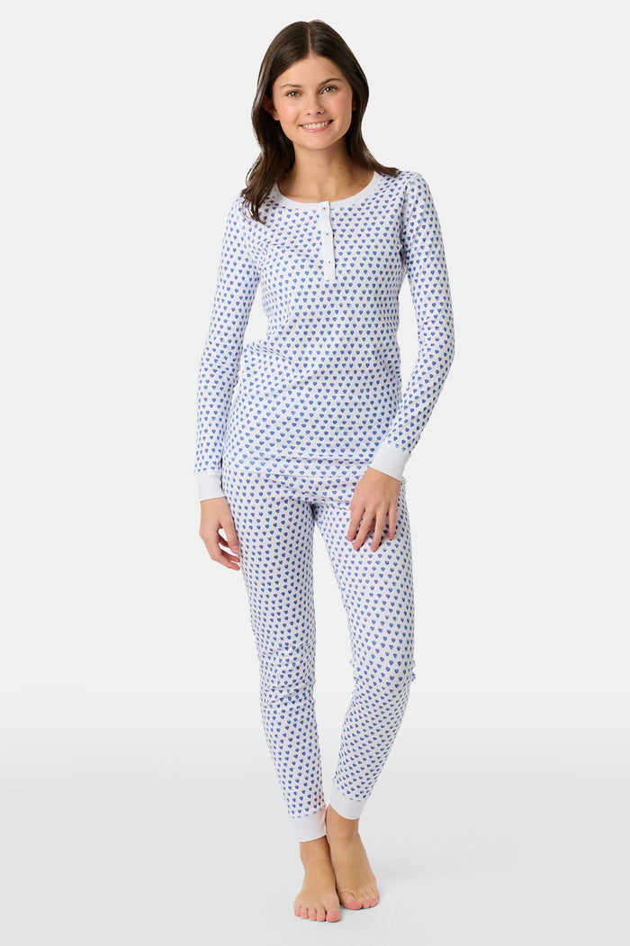 A girl smiles barefoot in Roller Rabbit’s Kids Hearts Pajamas, a matching set featuring a heart print, and poses against a plain white background.