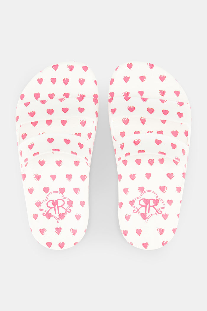 A pair of Kids Hearts Pool Slides by Roller Rabbit featuring an all-over pink heart pattern on a white background.