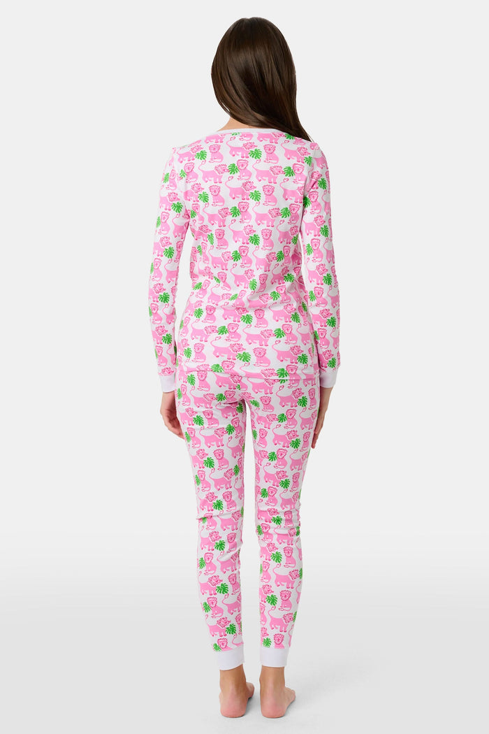 A young girl smiles barefoot against a white background in Roller Rabbit's Kids Leo The Lion Pajamas—soft Pima cotton, long sleeves, white cuffs, and a playful pink-and-green animal print.