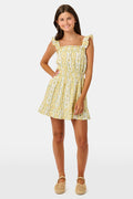 A girl wears the Roller Rabbit Kids Lillian Floral Stripe Tristan Dress, a cotton sundress with green and white stripes, floral patterns, ruffled straps, and a ruffled hem, standing with a smile and one arm relaxed at her side.