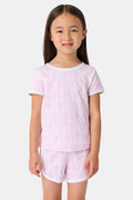 A young girl with straight brown hair wears the Roller Rabbit Kids Lovely Monkey Playa Play Set, a light pink Pima cotton pajama with short sleeves and shorts featuring a subtle monkey pattern as she smiles against a plain white background.