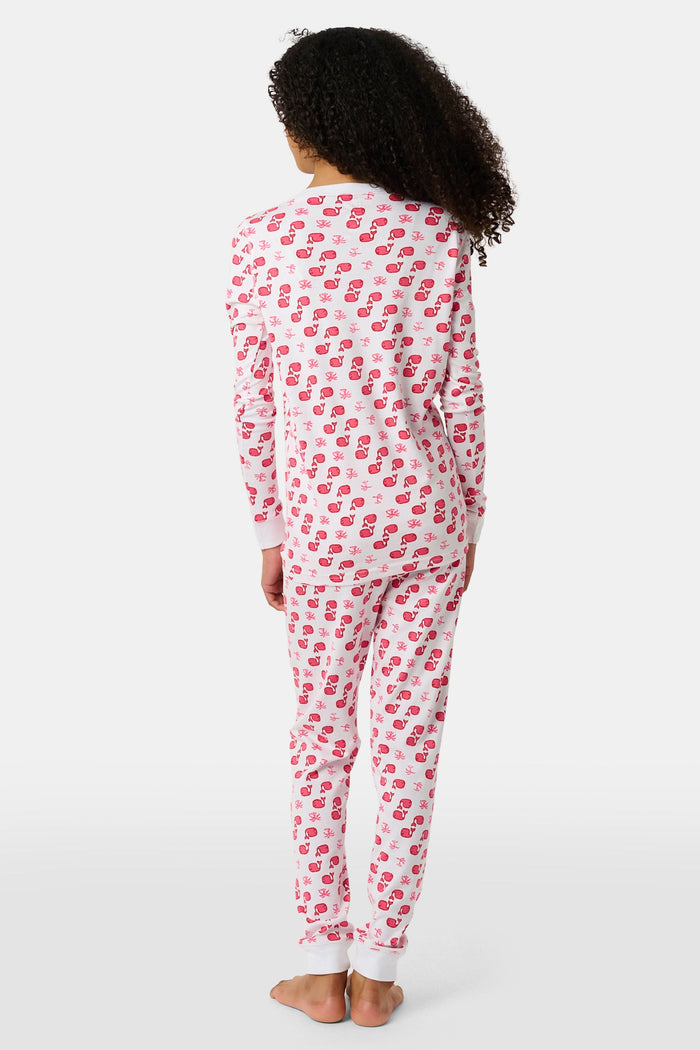 A young child with long brown hair stands barefoot, smiling and wearing the Roller Rabbit Kids Moby Pajamas made from soft Pima cotton, featuring a pink and red mitten pattern, against a plain light background.