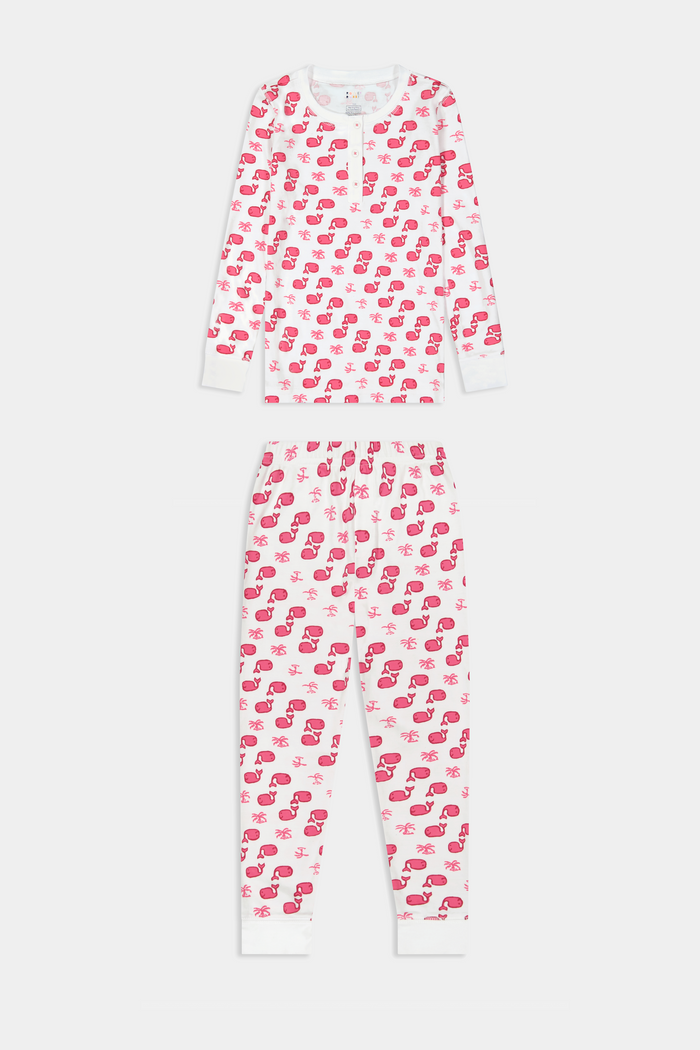 A young child with long brown hair stands barefoot, smiling and wearing the Roller Rabbit Kids Moby Pajamas made from soft Pima cotton, featuring a pink and red mitten pattern, against a plain light background.