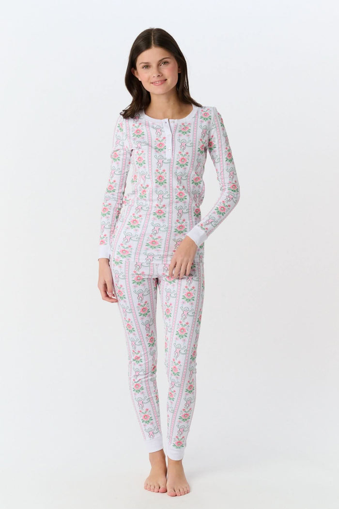 A young girl stands barefoot in Roller Rabbit Kids Monkey Block Stripe Pajamas—matching long-sleeve top and pants with playful monkey block stripes—smiling against a plain light gray background.