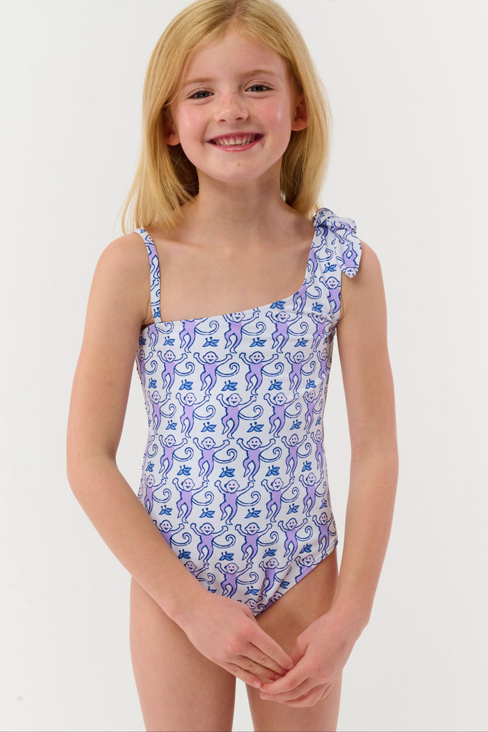 A girl wears the Roller Rabbit Kids Monkey Jacey One Piece with adjustable straps, standing under a palm tree, joyfully reaching for the clear blue sky while holding someone's hand.