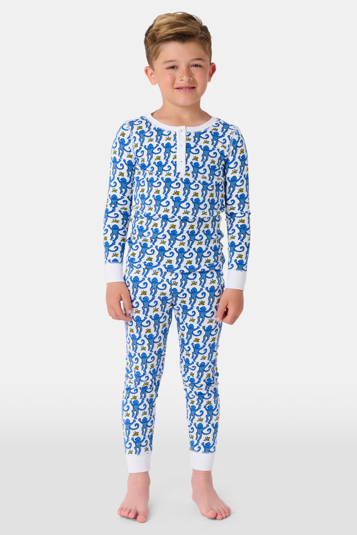 A young boy stands barefoot, smiling, and wearing Roller Rabbit Kids Monkey Pajamas—a matching top and bottom set. The background is plain white.