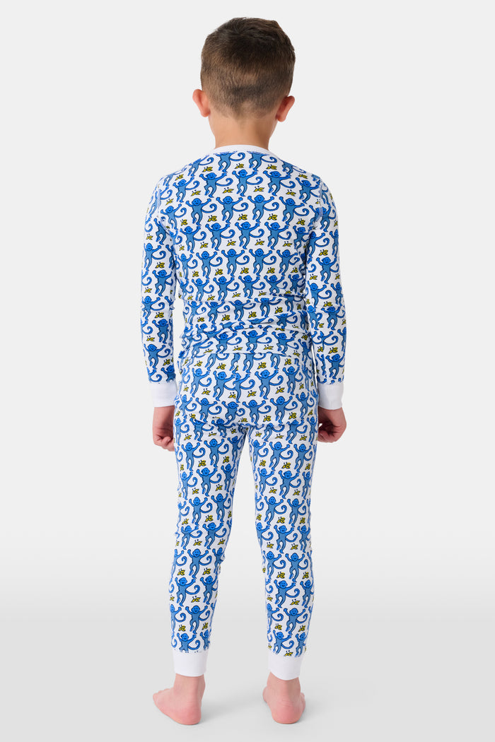 A young boy stands barefoot, smiling, and wearing Roller Rabbit Kids Monkey Pajamas—a matching top and bottom set. The background is plain white.