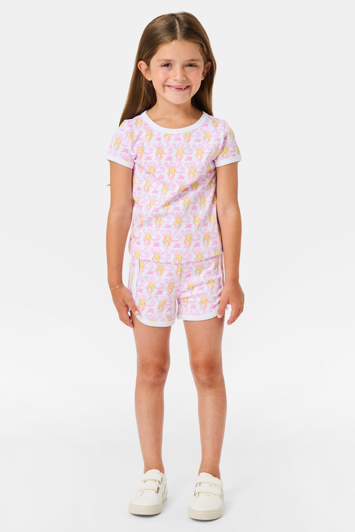 A young girl with long brown hair wears the Roller Rabbit Kids Monkey Playa Play Set and white shoes, standing and smiling against a plain white background.