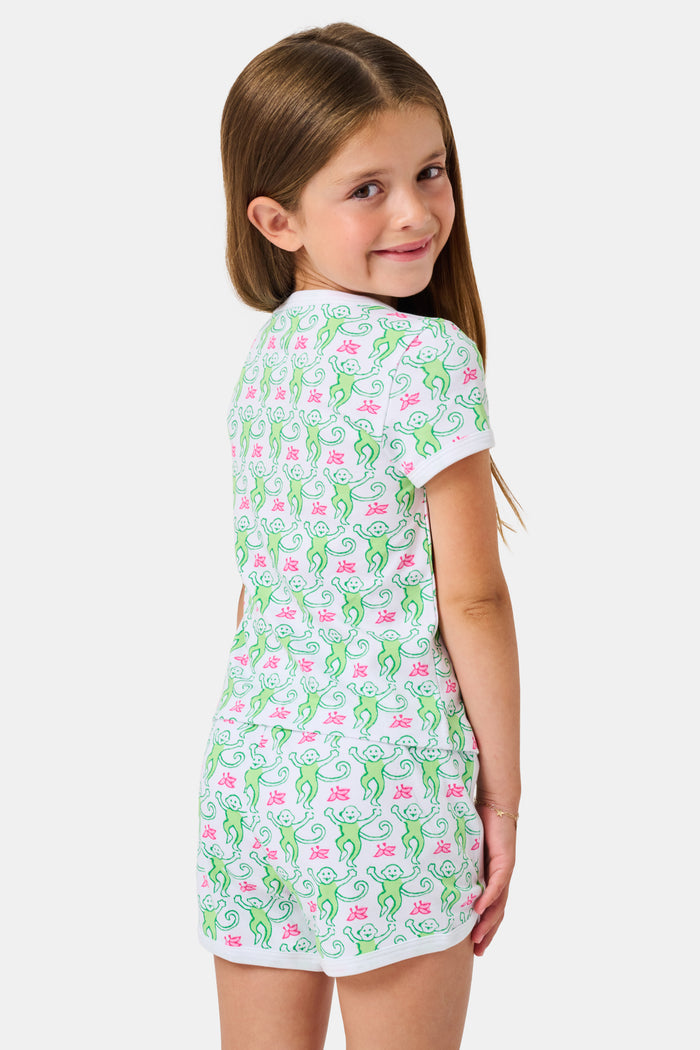 Smiling young girl with long brown hair wearing the Roller Rabbit Kids Monkey Playa Play Set and white shoes, standing against a plain white background.