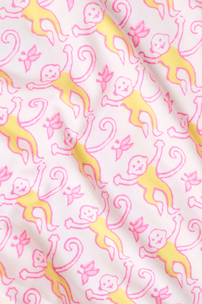 Introducing the Monkey Fiora Pajamas from Roller Rabbit—crafted from fabric adorned with a delightful pattern of pink and yellow monkeys with curled tails and smiling faces, interspersed with tiny leaves on a crisp white background. Perfect for adding playful charm to your sleepwear collection.