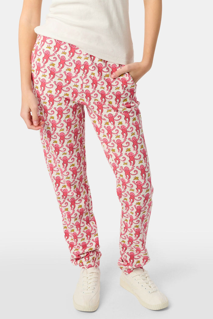 Wearing Roller Rabbit’s Kids Monkey Sweatpants featuring a playful monkey pattern and banded waistband, white sneakers, and a white top, a person stands with one hand in their pocket against a plain background.