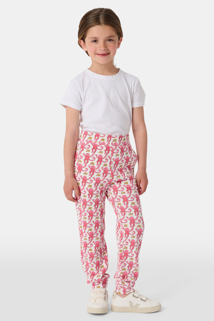 Wearing Roller Rabbit’s Kids Monkey Sweatpants featuring a playful monkey pattern and banded waistband, white sneakers, and a white top, a person stands with one hand in their pocket against a plain background.