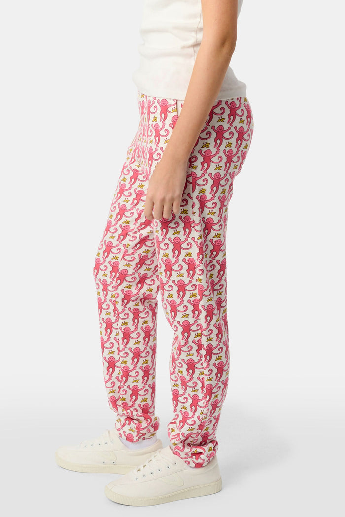 Wearing Roller Rabbit’s Kids Monkey Sweatpants featuring a playful monkey pattern and banded waistband, white sneakers, and a white top, a person stands with one hand in their pocket against a plain background.