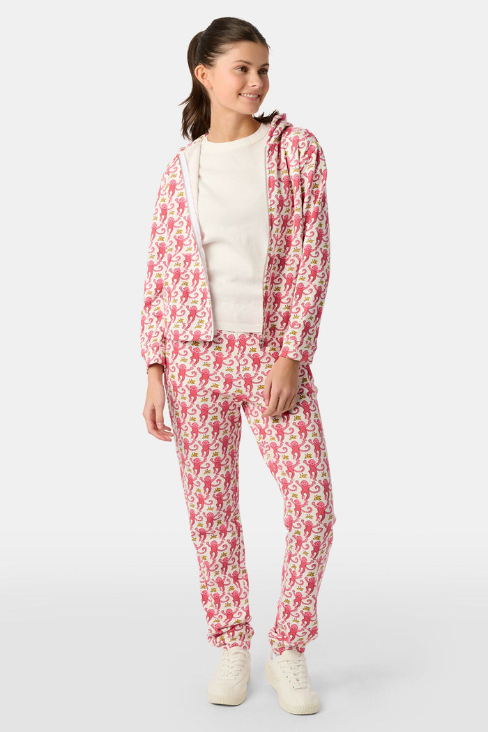 Wearing Roller Rabbit’s Kids Monkey Sweatpants featuring a playful monkey pattern and banded waistband, white sneakers, and a white top, a person stands with one hand in their pocket against a plain background.