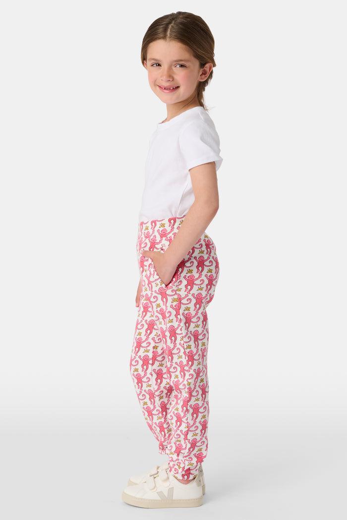 Wearing Roller Rabbit’s Kids Monkey Sweatpants featuring a playful monkey pattern and banded waistband, white sneakers, and a white top, a person stands with one hand in their pocket against a plain background.