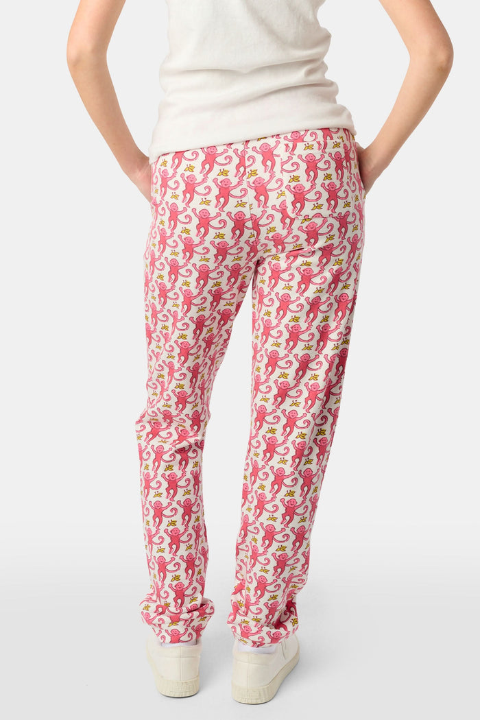 Wearing Roller Rabbit’s Kids Monkey Sweatpants featuring a playful monkey pattern and banded waistband, white sneakers, and a white top, a person stands with one hand in their pocket against a plain background.