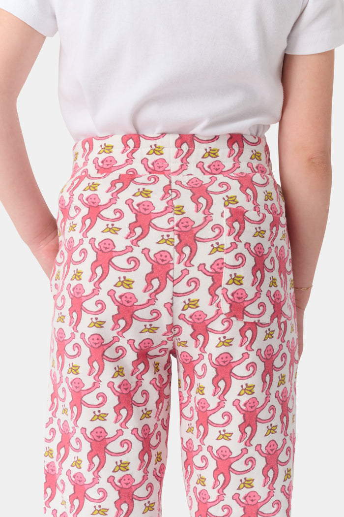 Wearing Roller Rabbit’s Kids Monkey Sweatpants featuring a playful monkey pattern and banded waistband, white sneakers, and a white top, a person stands with one hand in their pocket against a plain background.