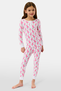 A young girl smiles barefoot in Roller Rabbit’s Kids Romy the Rabbit Pajamas, a soft Pima cotton long-sleeve set with a playful rabbit print; her brown hair frames her face against a simple, light background.
