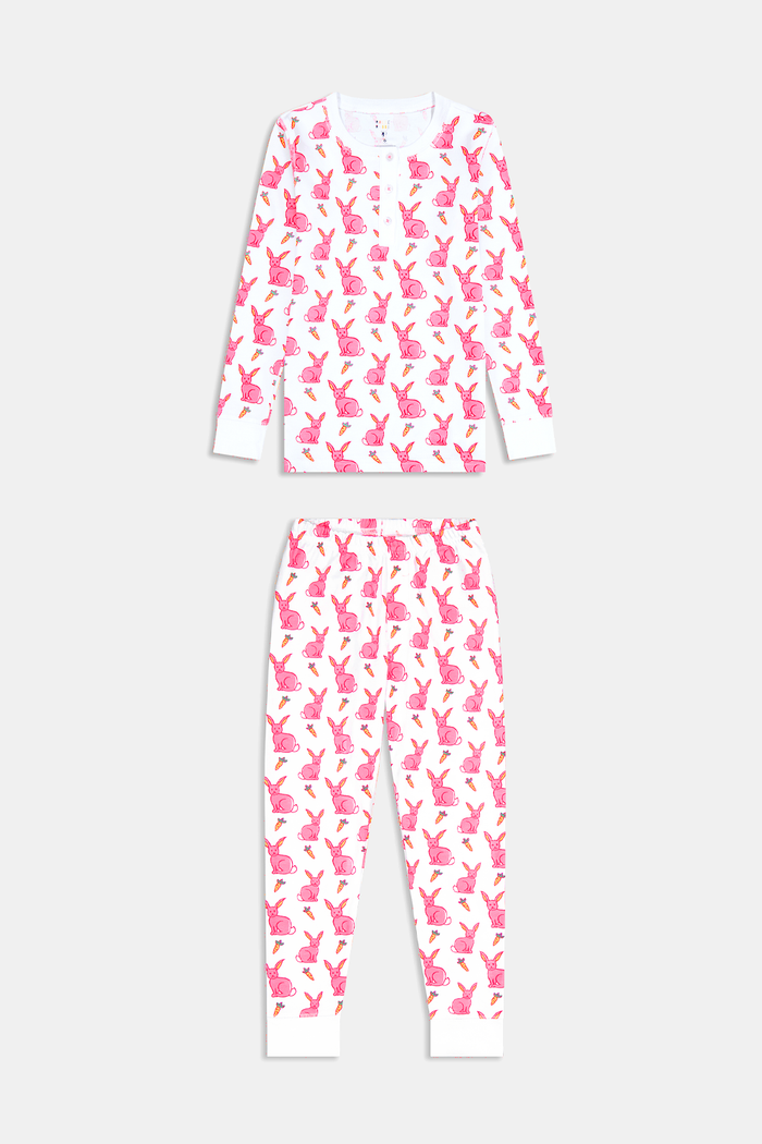 A young girl smiles barefoot in Roller Rabbit’s Kids Romy the Rabbit Pajamas, a soft Pima cotton long-sleeve set with a playful rabbit print; her brown hair frames her face against a simple, light background.