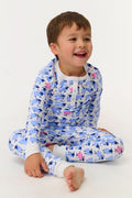 A young boy smiles on a white backdrop, wearing Roller Rabbit's Kids Sammy The Sheep Pajamas—cozy Pima cotton sleepwear featuring a playful sheep print, perfect for sweet dreams.