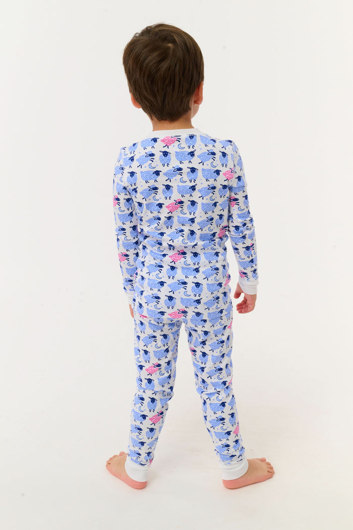 A young boy smiles on a white backdrop, wearing Roller Rabbit's Kids Sammy The Sheep Pajamas—cozy Pima cotton sleepwear featuring a playful sheep print, perfect for sweet dreams.