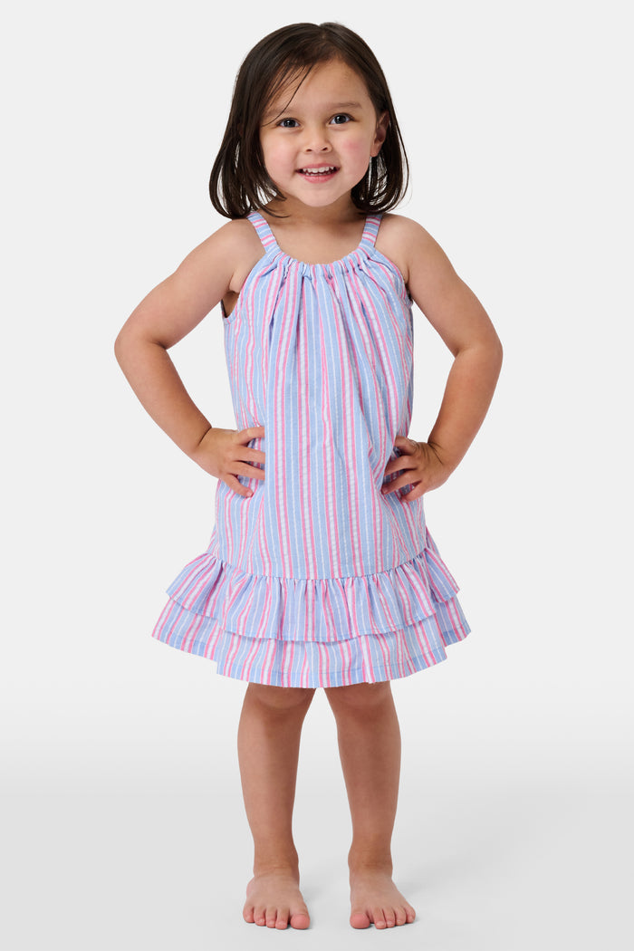A young girl wearing the Roller Rabbit Kids Sweet Stripe Casey Dress stands in front of lockers, smiling and holding a folder decorated with colorful raindrops.