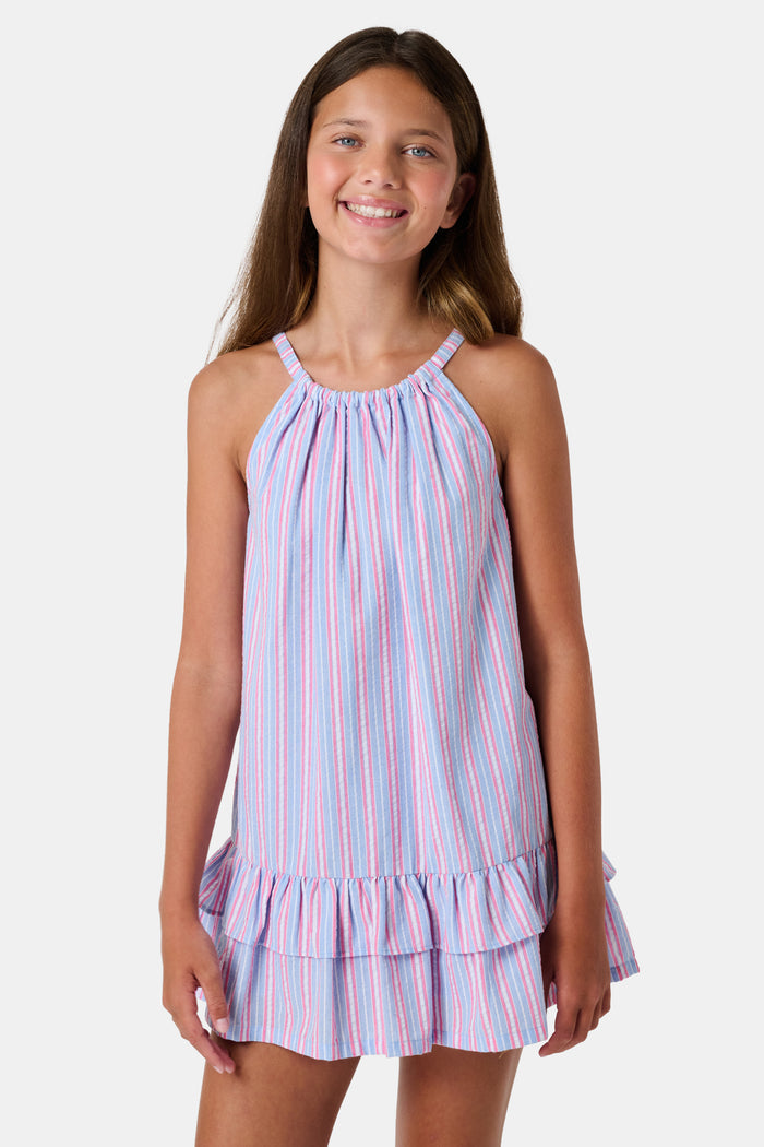 A young girl wearing the Roller Rabbit Kids Sweet Stripe Casey Dress stands in front of lockers, smiling and holding a folder decorated with colorful raindrops.