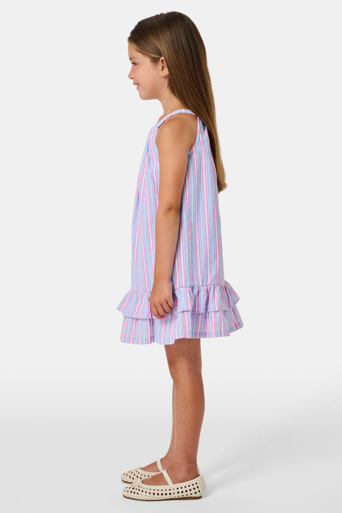 A young girl wearing the Roller Rabbit Kids Sweet Stripe Casey Dress stands in front of lockers, smiling and holding a folder decorated with colorful raindrops.