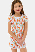 A young girl with long brown hair smiles in the Roller Rabbit Kids Teddy Tiger Playa Play Set, a white 100 Pima cotton outfit featuring colorful orange tiger and green plant patterns, standing against a plain light background.
